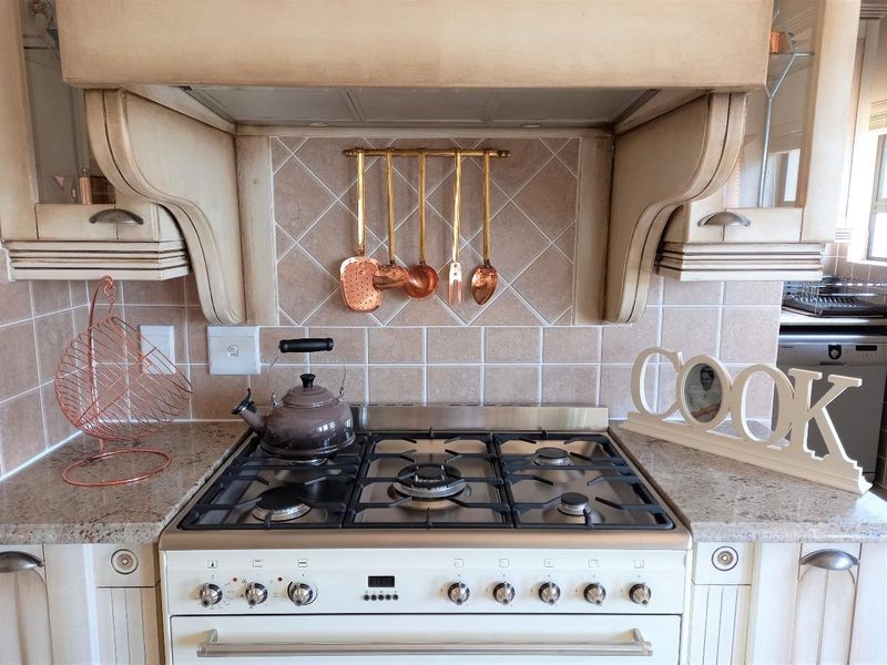 A well-maintained kitchen featuring a gas cooktop, integrated extractor fan, granite countertops, and classic tiled backsplash with custom cabinetry.