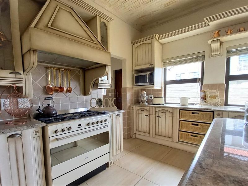 A well-appointed kitchen featuring classic cabinetry, stone countertops, a gas stove with an integrated extractor hood, and tiled flooring.