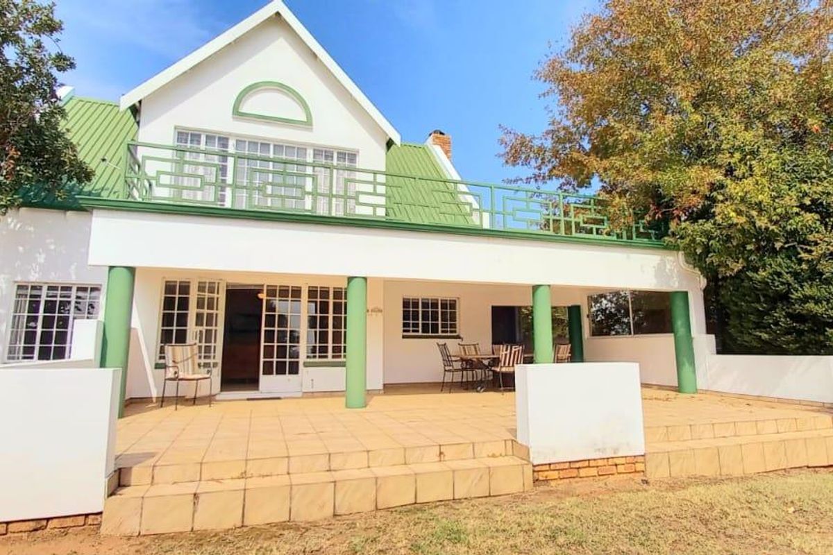 Rear view of the house featuring a spacious tiled patio, covered veranda, and an upper-level balcony with green metal roofing.