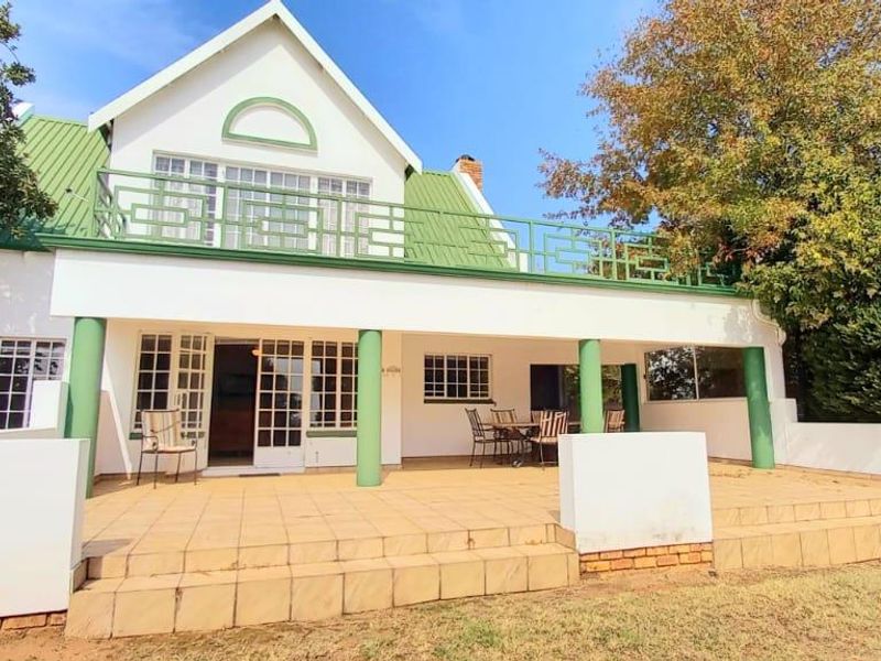 Rear view of the house featuring a spacious tiled patio, covered veranda, and an upper-level balcony with green metal roofing.