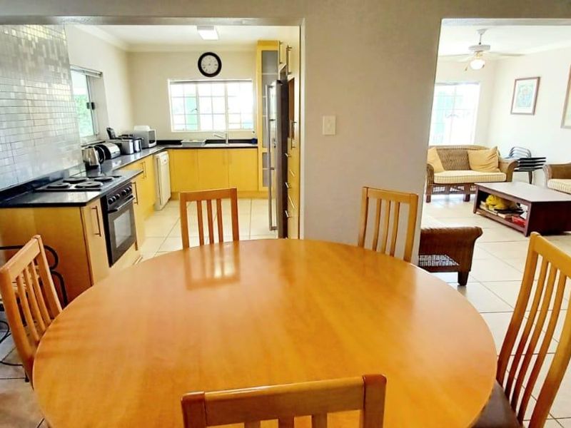 Open-plan kitchen and dining area featuring tiled floors, wooden cabinetry, and a mosaic backsplash, flowing into an adjacent living space.
