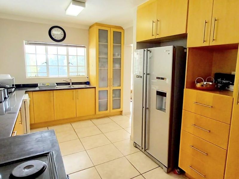 A functional kitchen featuring light wood cabinetry, tiled flooring, dark countertops, and a dedicated pantry cupboard with ample storage space.