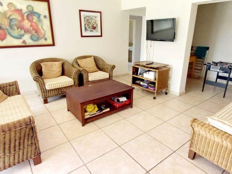 A living room area featuring neutral ceramic floor tiles and an open-plan layout leading to a staircase.
