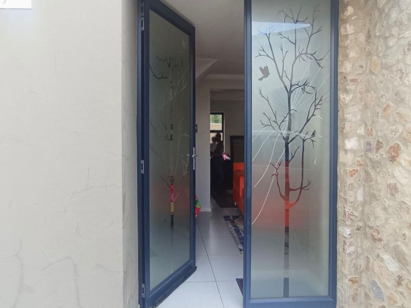 Main entrance featuring modern etched glass double doors, stone cladding accents, and tiled flooring leading into the home.