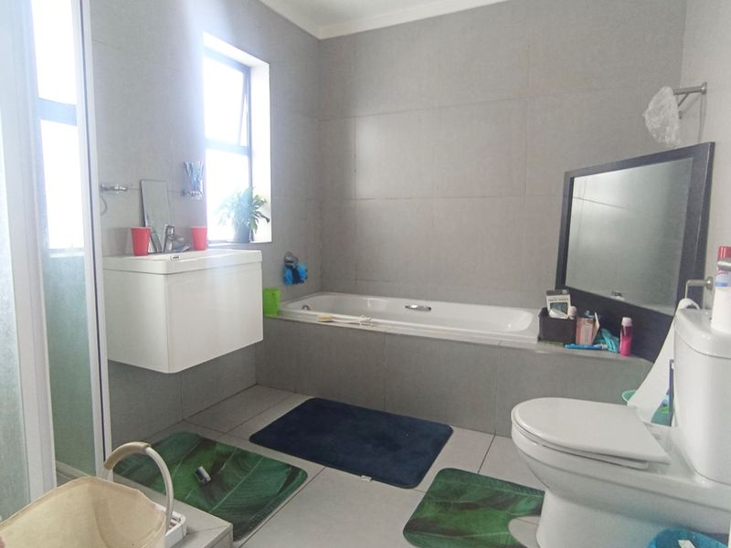 Modern bathroom featuring a wall-mounted vanity, built-in bathtub, separate shower enclosure, and neutral grey wall tiling throughout.