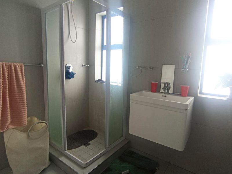 A functional bathroom featuring a corner shower enclosure, wall-mounted vanity unit, and neutral wall tiling with natural light from the window.