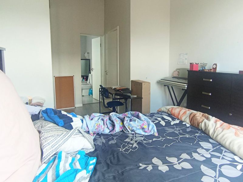 A bedroom featuring neutral walls and laminate flooring, with an adjoining en-suite bathroom visible through the doorway.