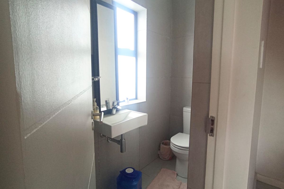 A compact, modern bathroom featuring a wall-mounted basin, chrome fixtures, and neutral wall tiling.