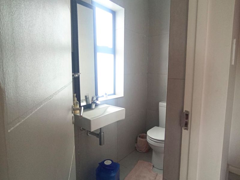 A compact, modern bathroom featuring a wall-mounted basin, chrome fixtures, and neutral wall tiling.