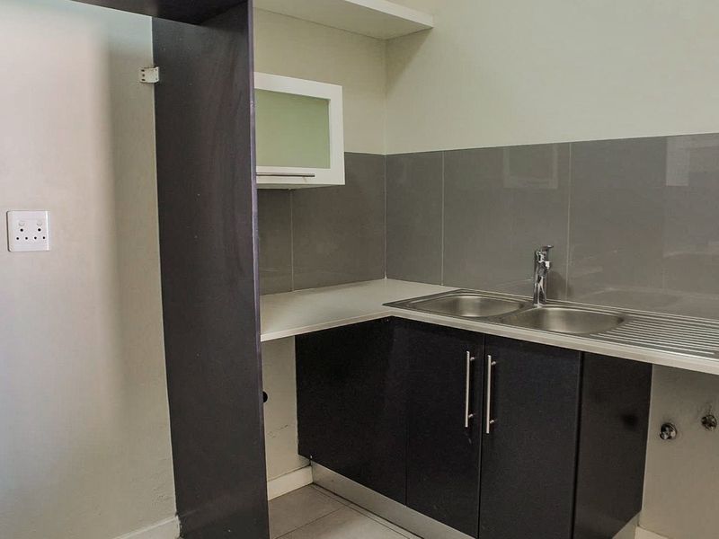 A compact, modern kitchen area featuring dark cabinetry, a stainless steel double sink, and a neutral tiled backsplash.