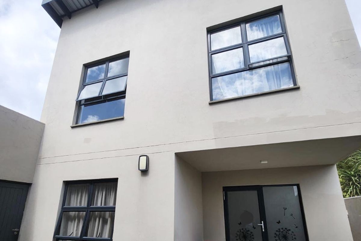 A view of the rear facade of a two-story house featuring modern aluminium window frames and a covered patio area.