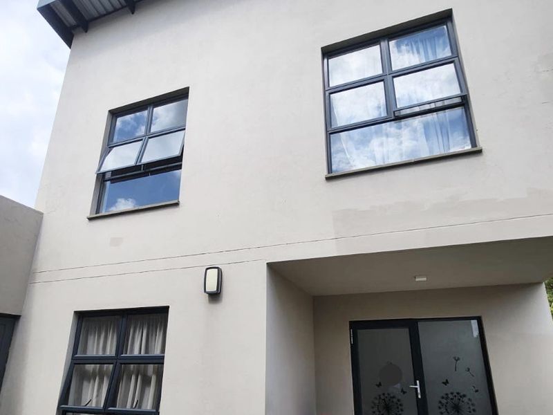 A view of the rear facade of a two-story house featuring modern aluminium window frames and a covered patio area.