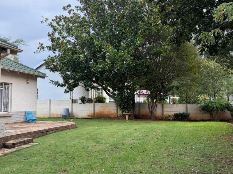 A spacious rear garden featuring a tiled patio area, established trees, and a secure precast concrete boundary wall.
