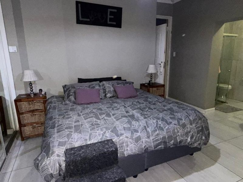 Spacious bedroom featuring tiled flooring, built-in wardrobe, and an open-plan en-suite bathroom equipped with a freestanding bathtub and glass shower enclosure.