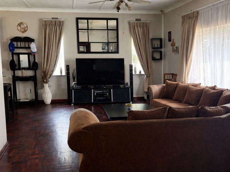 A comfortable living room featuring classic parquet flooring, a ceiling fan, and large windows with curtain rails, providing a warm and inviting atmosphere.