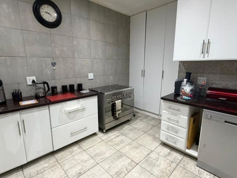 A functional kitchen featuring white cabinetry, dark laminate countertops, a stainless steel stove, tiled splashbacks, and tiled flooring.
