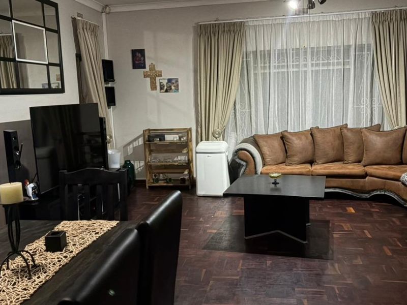 A comfortable living room featuring classic parquet flooring and large windows with curtain tracks, offering a warm and functional space for relaxation.