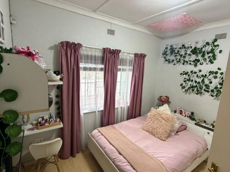 A cozy bedroom featuring laminate flooring, security bars on the windows, and classic ceiling cornicing.