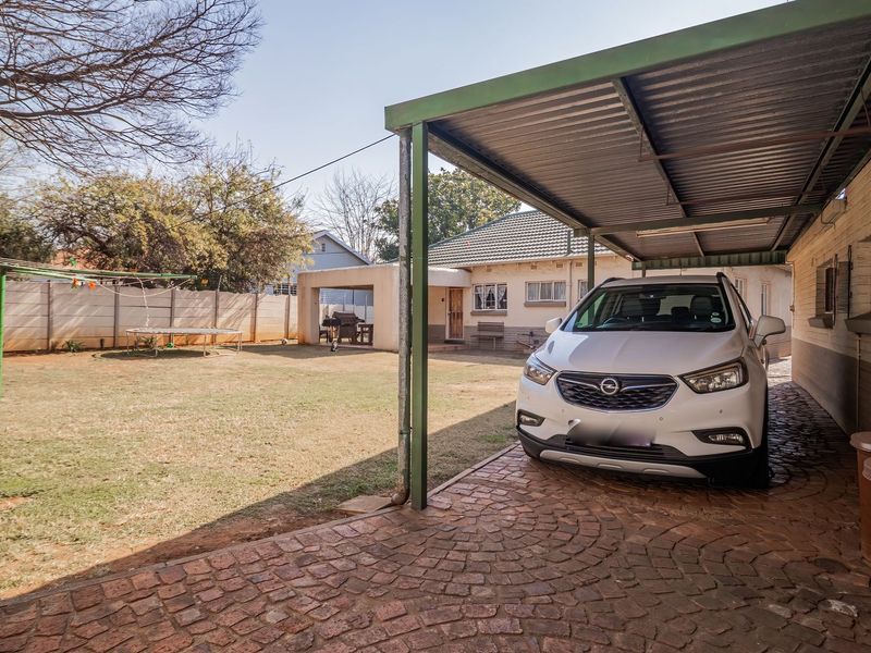 Rear exterior view featuring a paved carport, spacious lawn, and perimeter walling, providing a functional outdoor area.