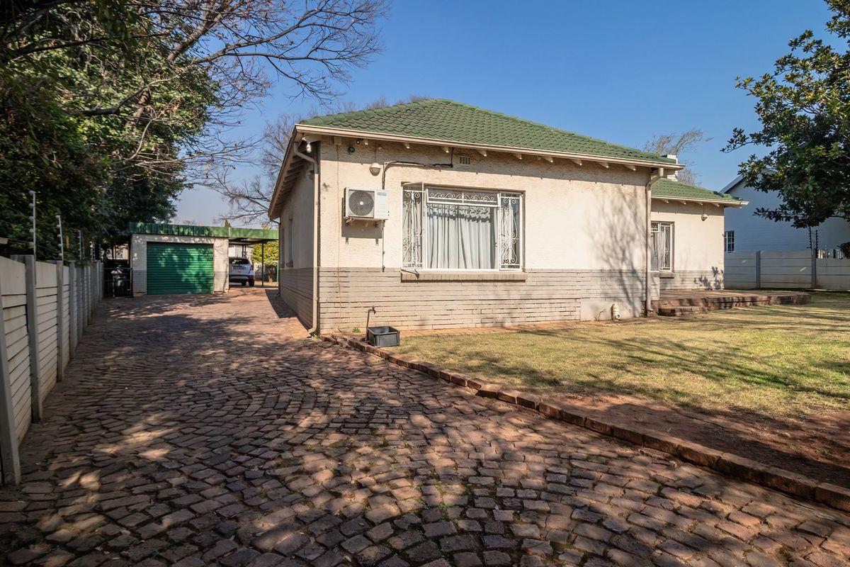 Rear view of the property featuring a cobblestone driveway, green tiled roof, and a detached garage set within a fenced garden area.
