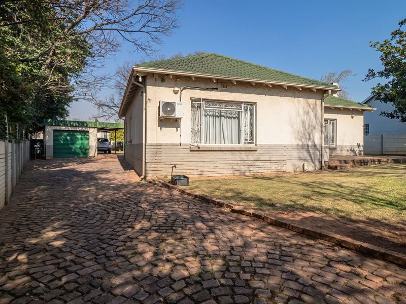 Rear view of the property featuring a cobblestone driveway, green tiled roof, and a detached garage set within a fenced garden area.