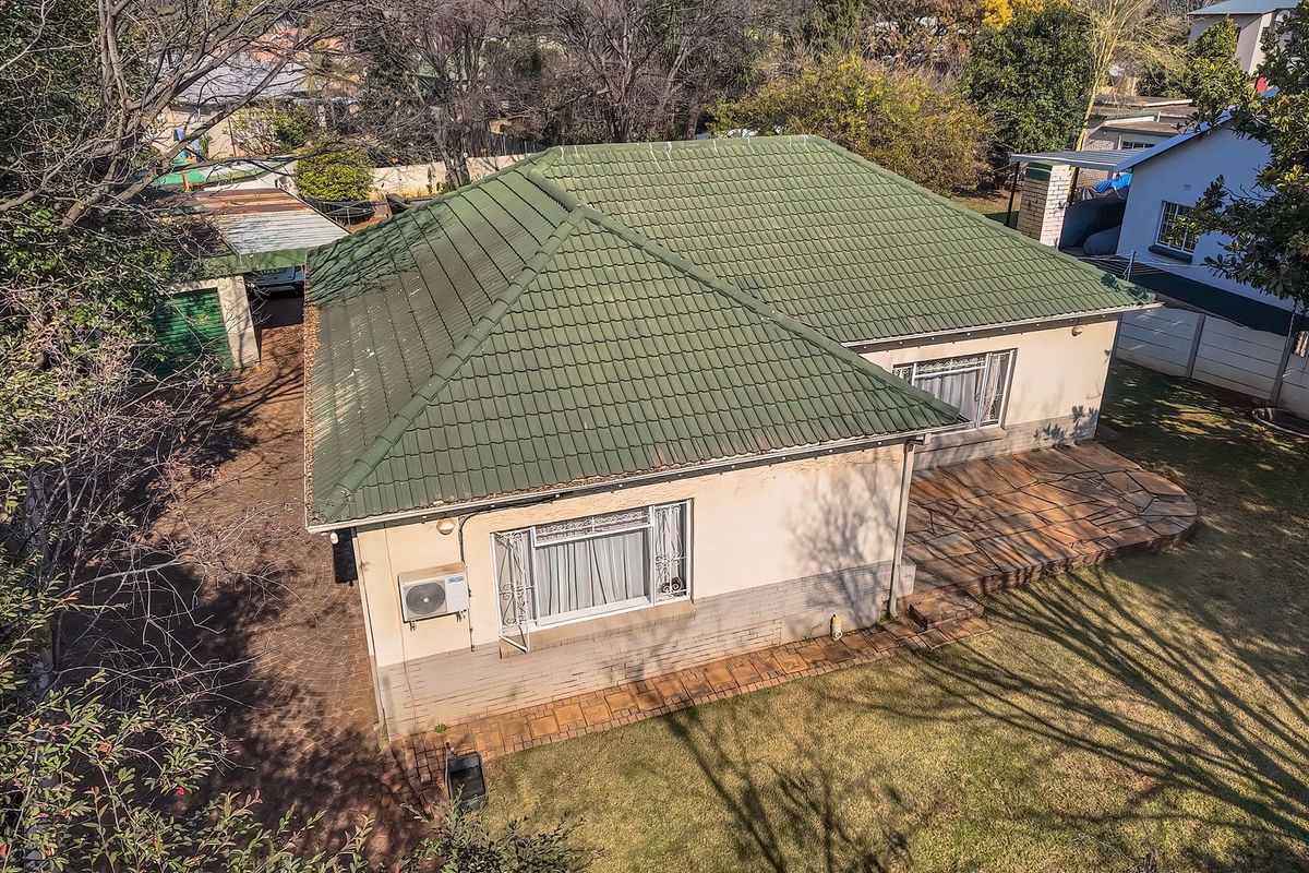 Aerial view of the property featuring a tiled roof, stone patio area, and paved driveway set within a landscaped garden.