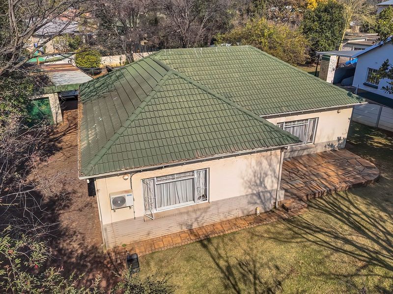 Aerial view of the property featuring a tiled roof, stone patio area, and paved driveway set within a landscaped garden.