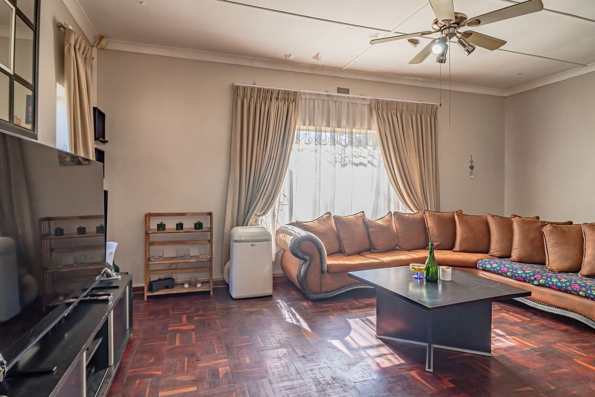 A spacious living room featuring classic parquet flooring, a ceiling fan, and large windows with curtain rails, offering a comfortable and functional living space.