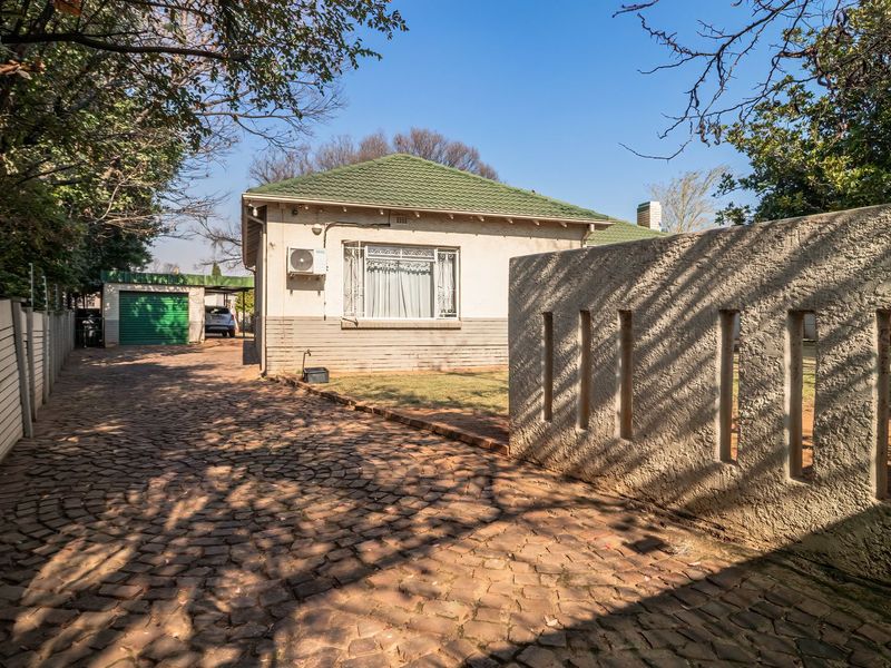 Front view of a house featuring a cobblestone driveway, concrete boundary wall, electric fencing, and a detached garage.
