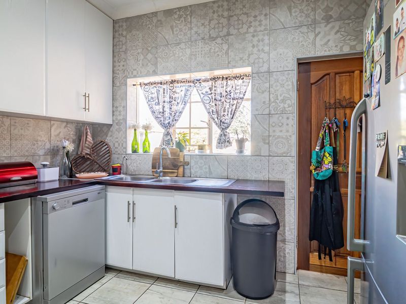 A functional kitchen featuring white cabinetry, patterned tiled backsplash, laminate countertops, and a stainless steel sink with tiled flooring.