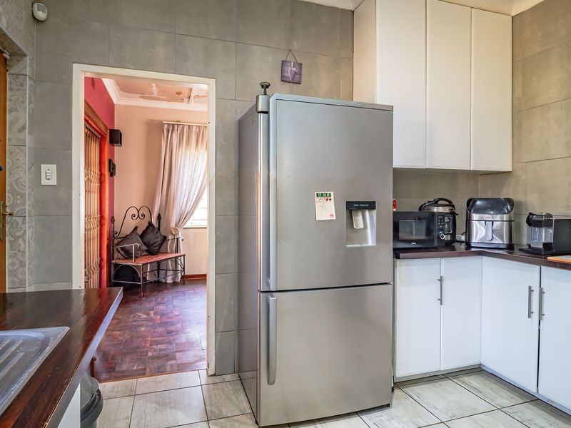 A functional kitchen featuring white cabinetry, tiled splashbacks, and tiled flooring, with a doorway leading to an adjacent living area.