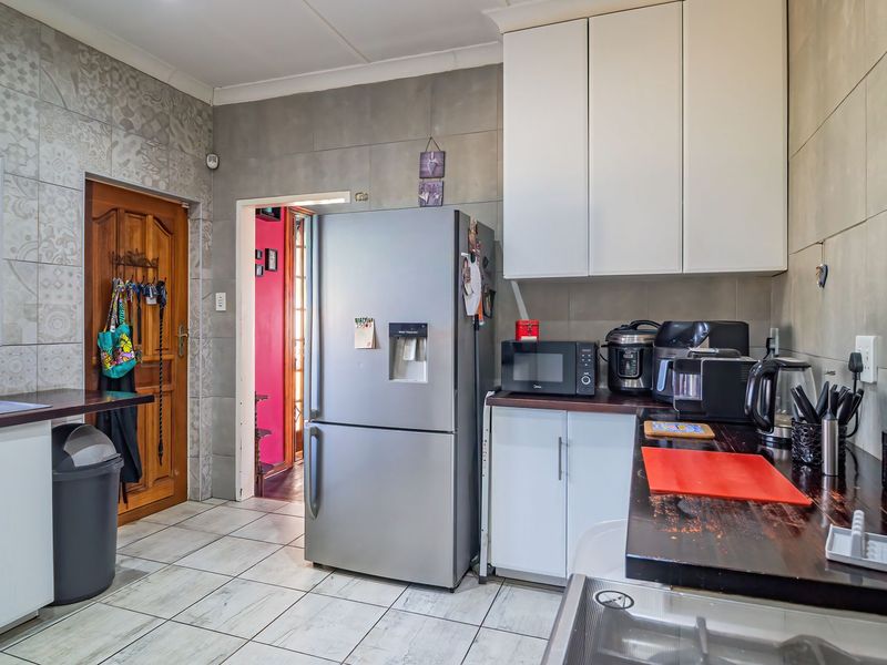 A functional kitchen featuring tiled walls, white cabinetry, dark countertops, and tiled flooring, providing a practical workspace with direct access to adjacent rooms.