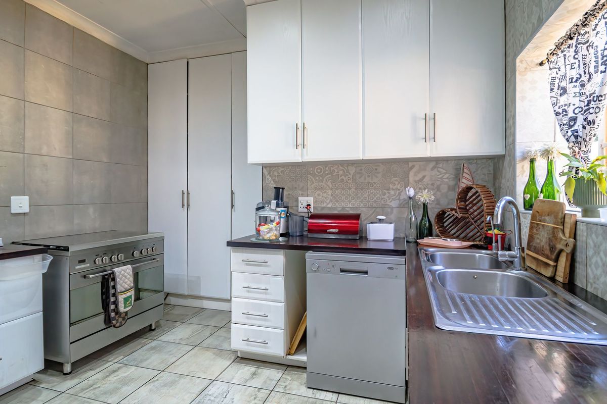 A functional kitchen featuring white cabinetry, stainless steel stove, double sink, and tiled splashback with neutral floor tiles.