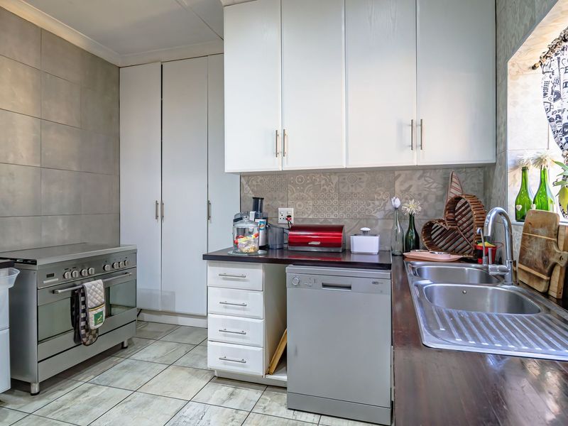 A functional kitchen featuring white cabinetry, stainless steel stove, double sink, and tiled splashback with neutral floor tiles.