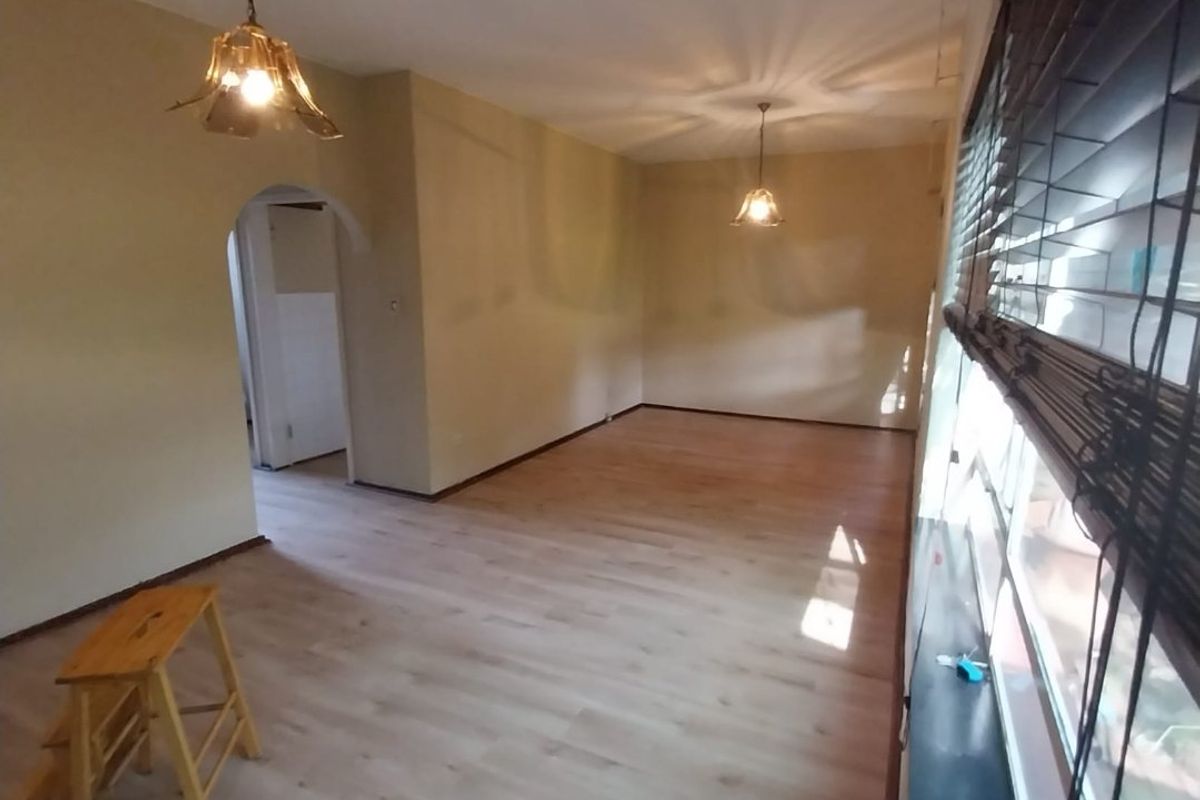 A spacious, empty living area featuring light-toned laminate flooring, an architectural archway, and large windows fitted with venetian blinds.