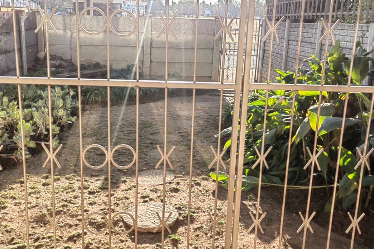 A small, enclosed rear garden area featuring a metal security gate, perimeter walling, and established garden beds.
