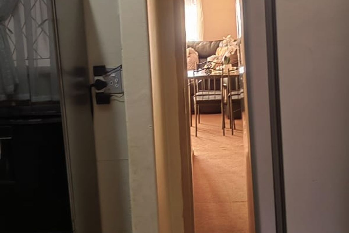 A view from a tiled kitchen area looking through a doorway into an adjacent living space with carpeted flooring.