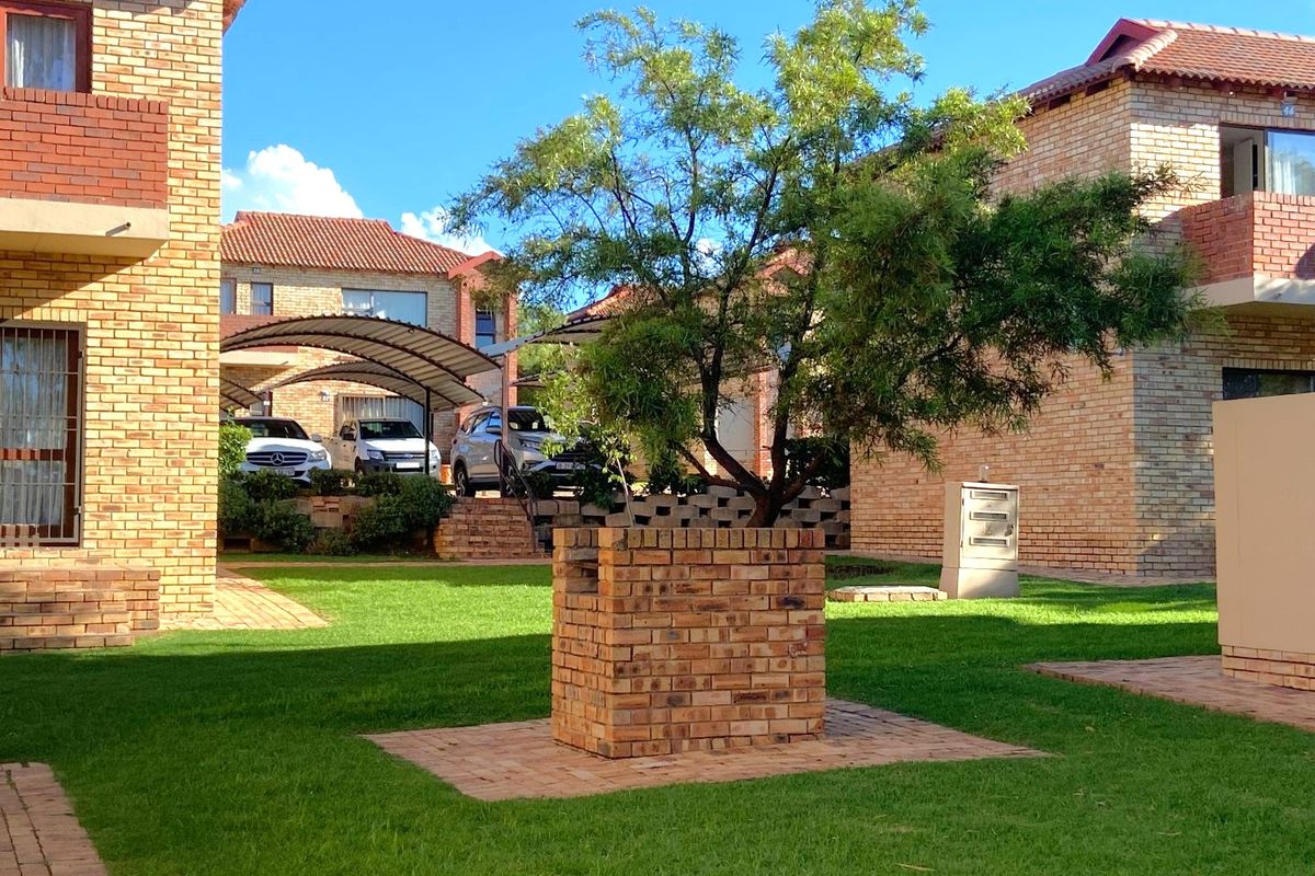 A well-maintained communal garden area featuring face brick apartment buildings, paved walkways, and a covered carport structure.