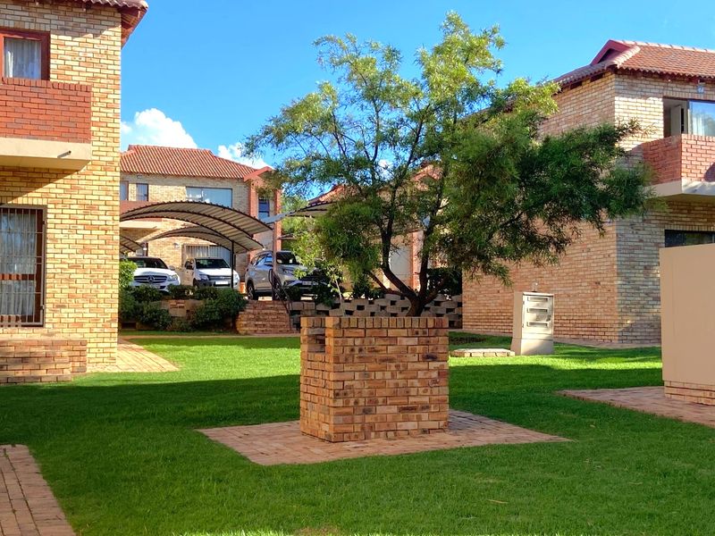 A well-maintained communal garden area featuring face brick apartment buildings, paved walkways, and a covered carport structure.