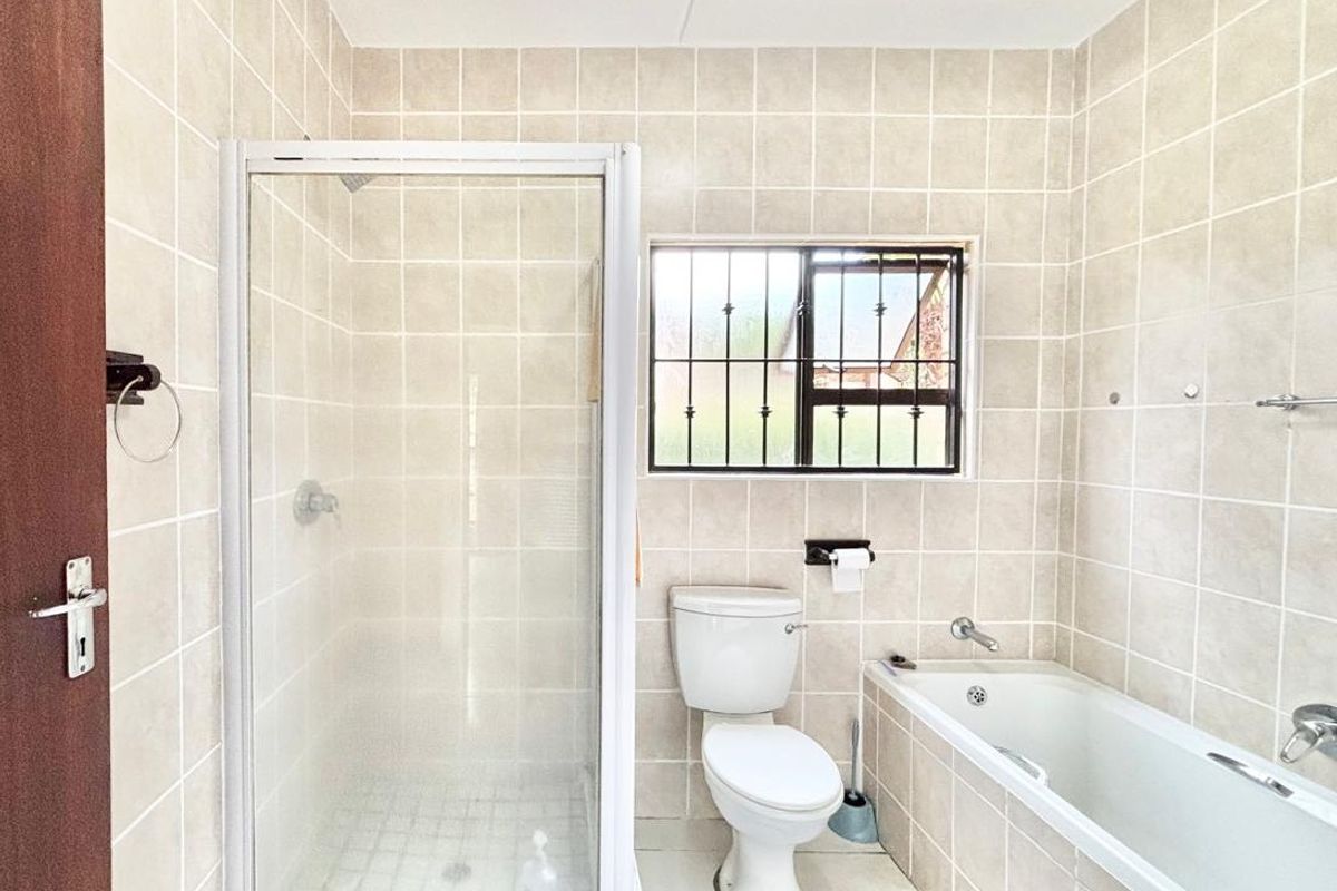 A functional bathroom featuring a separate shower enclosure, bathtub, toilet, and vanity countertop with neutral wall tiling and security bars on the window.