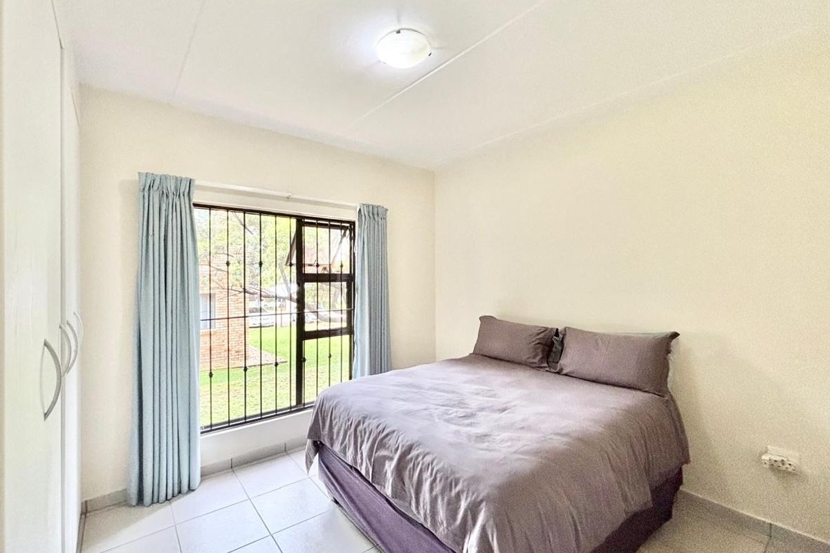 A functional bedroom featuring tiled flooring, a built-in wardrobe, and a window fitted with security bars, offering a clean and simple living space.