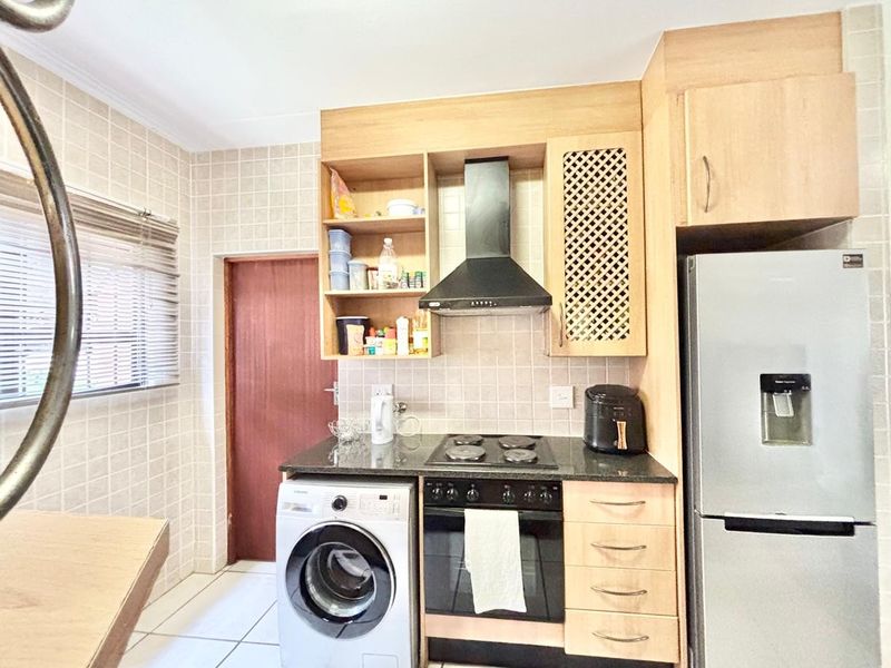 A functional kitchen featuring light wood cabinetry, granite countertops, a built-in oven and hob, extractor fan, and tiled finishes throughout.