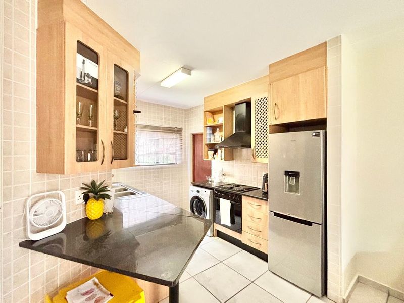 A functional kitchen featuring light wood cabinetry, granite countertops, a built-in oven with extractor fan, and tiled finishes throughout.