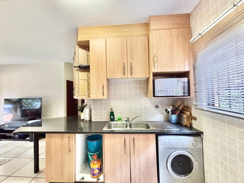 A functional kitchen featuring light wood-tone cabinetry, granite countertops, a stainless steel double sink, and a built-in microwave with an integrated washing machine.