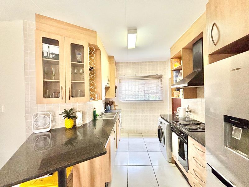 A functional galley-style kitchen featuring light wood cabinetry, granite countertops, tiled backsplash, and integrated appliances including an oven and hob.