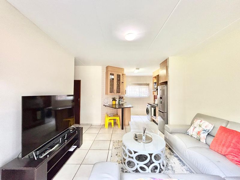 Open-plan living area featuring tiled flooring and a functional kitchen with built-in cabinetry, breakfast bar, and integrated appliance space.