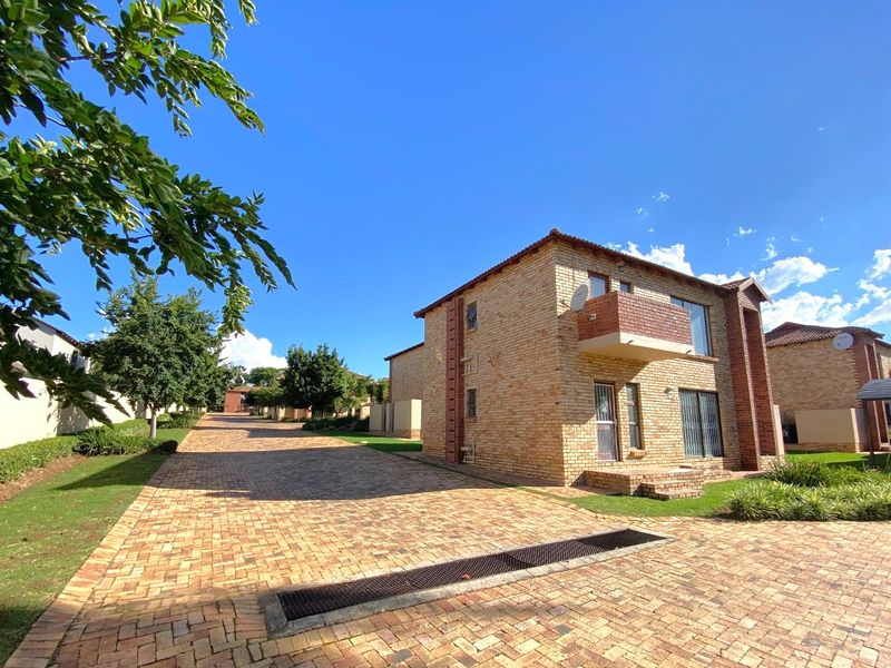 A view of a face brick apartment building featuring a paved driveway, balcony, and well-maintained exterior grounds.