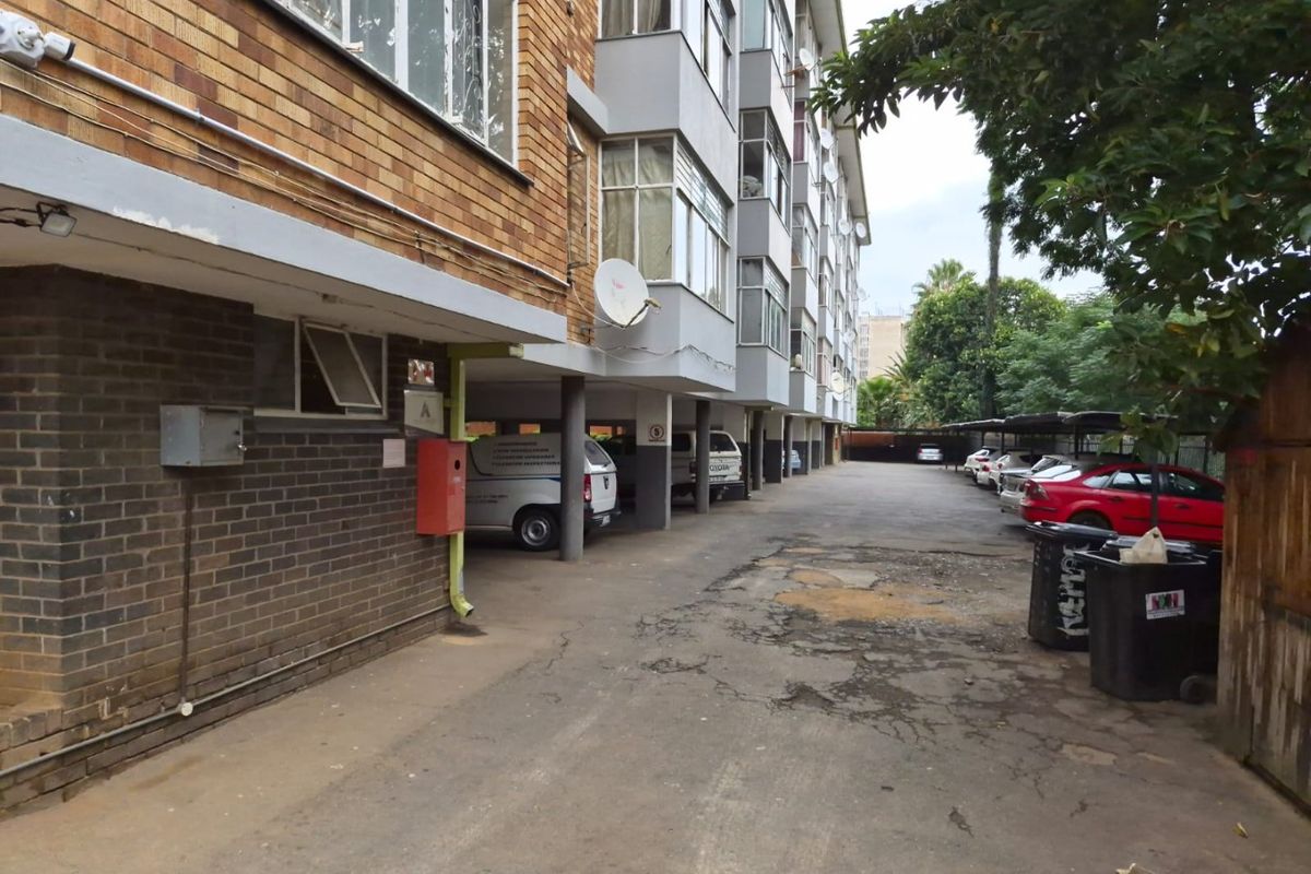 Rear exterior view of the apartment building featuring covered parking bays and a paved driveway area.