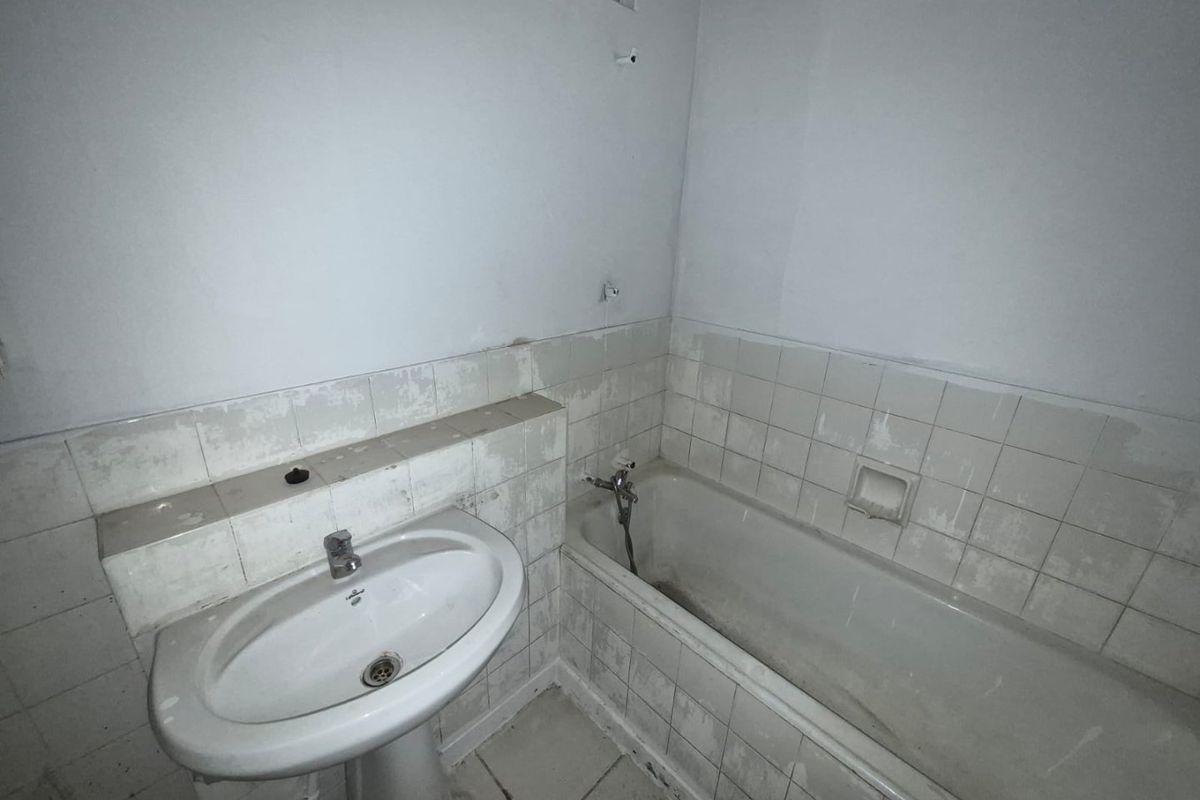 A dated bathroom featuring a pedestal basin and bathtub with worn wall tiling, requiring renovation to update the finishes and fixtures.