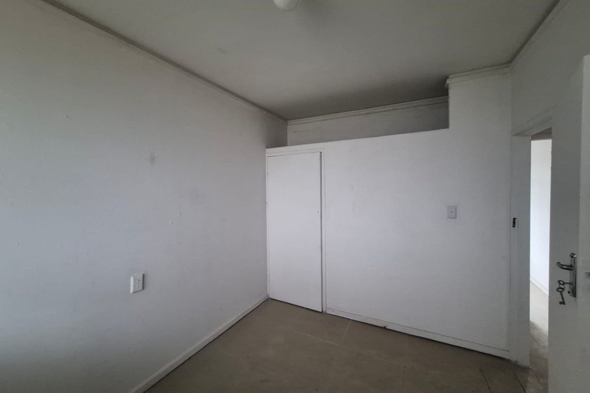 An empty bedroom featuring a built-in cupboard, neutral walls, and tiled flooring, offering a blank canvas for renovation or interior design updates.